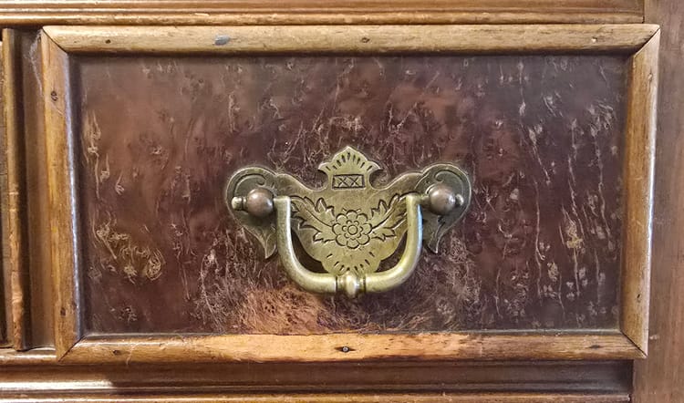 A close-up of the front of a drawer. Dark wood, engraved brass pull, deep scratches in the wood below.