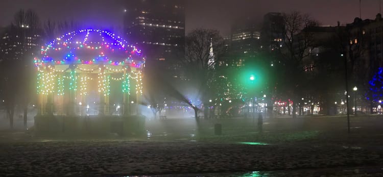 Boston Common bandstand at night, Christmas lights, fog billowing around from rapid snowmelt w/ eerie tree & people shadows.