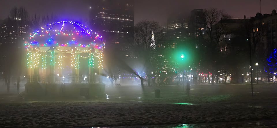 Boston Common bandstand at night, Christmas lights, fog billowing around from rapid snowmelt w/ eerie tree & people shadows.